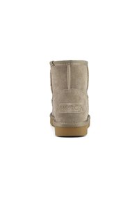 Stivale alla caviglia in suede beige con una superficie morbida, dettagli cuciti, suola in gomma piatta e marchio sul retro. Presenta un bordo superiore arrotondato.