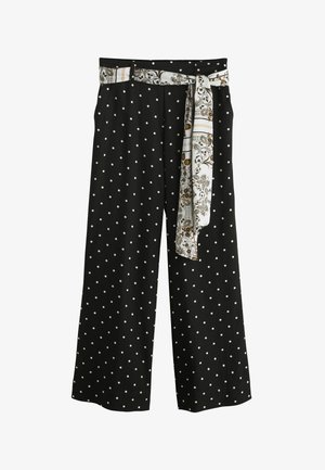 Persona che indossa pantaloni neri con pois bianchi e cintura a foulard fantasia, abbinati a un top corto nero.