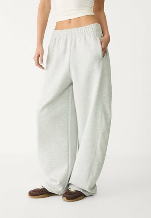 Pantaloni della tuta grigi chiari con vita elasticizzata, tasche laterali e vestibilità ampia. Realizzati in tessuto morbido e strutturato; presentano cuciture sottili.