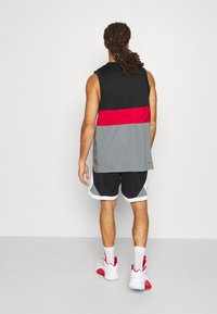 Conjunto deportivo que incluye una camiseta sin mangas negra con detalles en rojo y gris, combinada con pantalones cortos negros y zapatillas blancas con detalles en rojo.