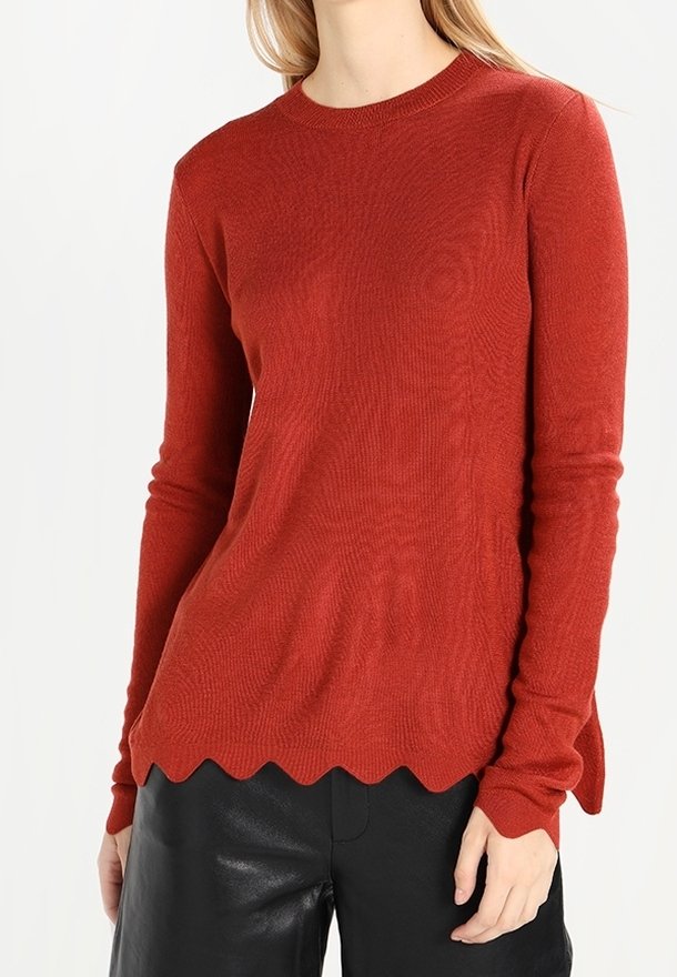 Roter Strickpulli mit rundem Halsausschnitt und gewelltem Saum. Hat lange Ärmel und einen weichen, strukturierten Stoff. Kombiniert mit schwarzen Lederhosen.