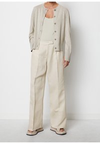 Jasnobeżowy kardigan na guziki, noszony na dopasowaną koszulkę na ramiączkach. Kremowe spodnie o szerokich nogawkach z zakładkami, zestawione z masywnymi beżowymi sandałami.