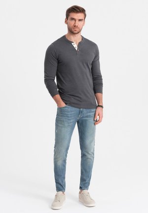 Grijs henley-shirt met lange mouwen en een placket met twee knopen, gecombineerd met lichtblauwe slim-fit jeans en beige sneakers.