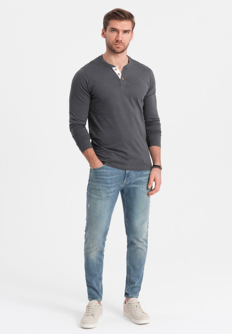 Langarm-Graues Henley-Shirt mit einer Zweiknopf-Leiste, kombiniert mit hellblauen Slim-Fit-Jeans und beigen Sneakers.