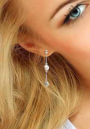 Des boucles d'oreilles en argent présentent une perle ronde et un charm en forme de feuille, suspendus par une délicate chaîne. Le design est élégant et léger.