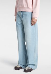 Jeans a gamba larga blu chiaro con vita alta e tasche frontali, abbinati a sneakers multicolore e una felpa rosa.