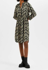 Robe noire et crème à motifs avec un col, des manches longues et une taille élastique. Design en chevrons notable et tissu texturé.