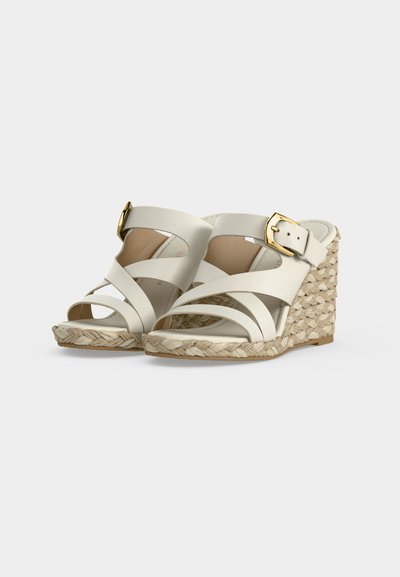 Sandales compensées blanches avec talons en corde tressée et brides à boucle dorée, présentées sur un fond uni gris clair.