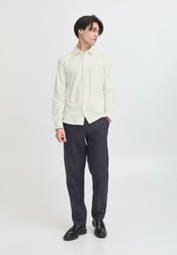 Light cream button-up shirt with a collar, paired with dark, loose-fitting trousers and black shoes. Simple, textured fabric design.