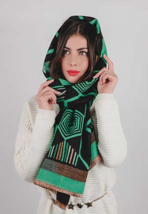 Sciarpa nera con audaci motivi geometrici verdi, bordi frangiati e dettagli in bronzo, indossata sopra un maglione chiaro.