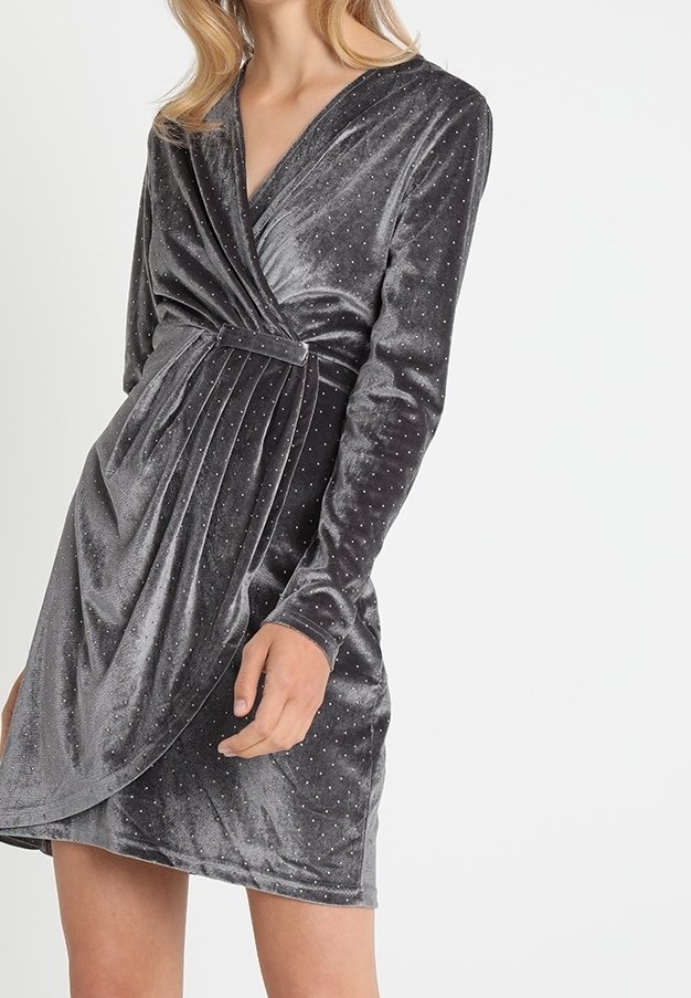 Femme portant une robe portefeuille en velours gris foncé ajustée, à manches longues et petites décorations scintillantes.