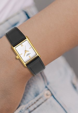 Gold rectangular watch with a white textured dial, black leather strap, and minimalist gold accents. Features a crown for adjusting time.