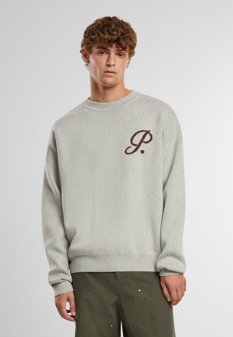 Sudadera de punto gris claro con cuello redondo, con una letra "P." en marrón oscuro en el pecho y puños y dobladillo de canalé.