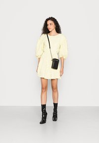 Vestido amarelo texturizado com mangas bufantes, cintura ajustada e saia ampla; combinado com botas pretas brilhantes até o tornozelo e uma pequena bolsa de ombro preta.