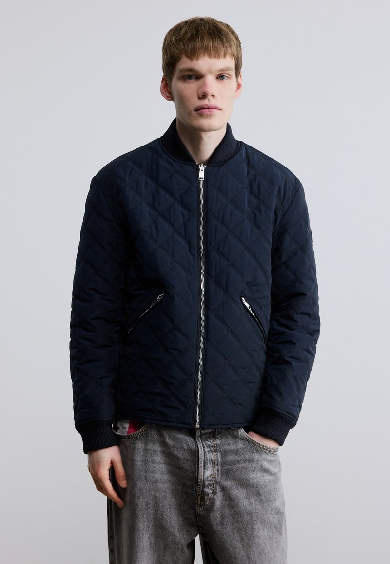 Καπιτονέ ναυτικό μπουφάν bomber με ριμπ γιακά και μανσέτες, διαθέτει δύο πλαϊνές τσέπες με φερμουάρ και λεία, υφή με υφή.