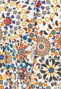 Tejido colorido con intrincados patrones de mariposas, flores y estrellas en naranja, azul, amarillo y negro sobre un fondo blanco.
