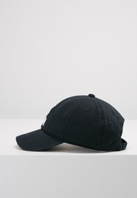 Zwarte katoenen baseballcap met gebogen rand, zes panelen, geborduurde luchtgaten en verstelbare strap aan de achterkant. Eenvoudig ontwerp zonder patronen.