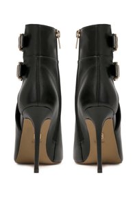 Botines de cuero negros de tacón alto, con dos cremalleras laterales, hebillas ajustables y un tacón de aguja afinado. Textura suave, diseño minimalista.