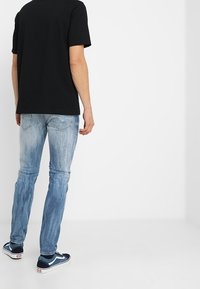 Musta lyhythihainen t-paita yhdistettynä vaaleansinisiin farkkuihin ja laivastonsinisiin lenkkareihin, joissa on valkoisia yksityiskohtia. Asusteena slim fit -leikkaus ja haalistunut pinta.