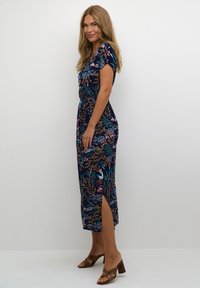 Vestido de flores en color navy con mangas cortas, cintura fruncida y aberturas laterales. Combinado con sandalias de tacón marrones. Textura de tela suave.
