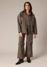 Veste en jean imprimée léopard et pantalon évasé assorti dans des tons terreux. Tissu texturé avec deux poches sur la veste et une coupe ajustée.