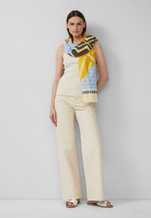 Débardeur crème et pantalon beige à pattes larges, associés à une écharpe à motifs en jaune, bleu et vert olive, drapée élégamment autour du cou.