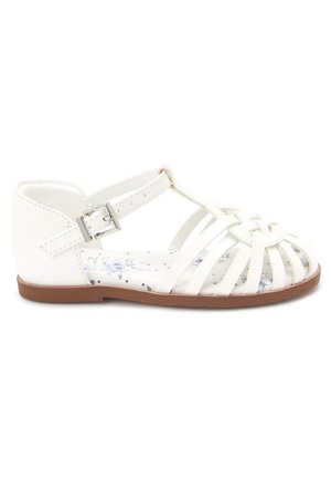 Sandales synthétiques blanches avec un design de brides croisées, une boucle de cheville ajustable et une semelle intérieure à motif floral sur une semelle en caoutchouc marron.