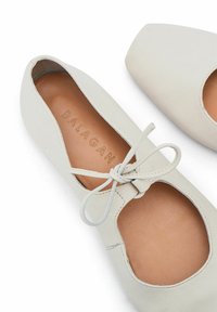 Ballerine in pelle bianca con punta tonda, design con fori e dettaglio a fiocco sul davanti, dotate di una soletta in pelle naturale.