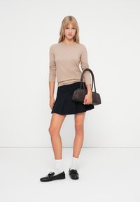 Beżowy sweter z długim rękawem, niebieska spódnica w kształcie dzwonu, czarne mokasyny, białe skarpetki i mała ciemna torebka. Prosty fason, miękka tekstura i dopasowany krój.