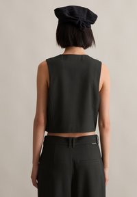 Schwarzes, ärmelloses Crop-Top aus strukturiertem Stoff mit dezenten vertikalen Streifen, kombiniert mit taillierten, hochgeschnittenen Hosen und einer schwarzen Kappe.