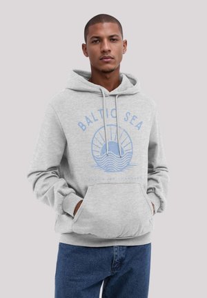 Grauer Hoodie mit einer Fronttasche, versehen mit einem blauen Druck eines Schiffs und Wellen, darüber mit der Beschriftung "BALTIC SEA". Getragen mit blauen Jeans.