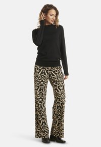 Black sweater with a high neck, paired with wide-legged trousers featuring a cream floral pattern on a black background. Black ankle boots.