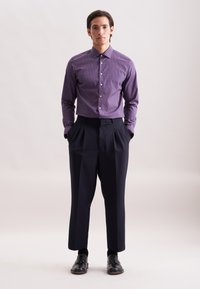 Camicia a righe viola, pantaloni scuri su misura e scarpe nere. La camicia presenta un design geometrico e bottoni sulla parte anteriore.