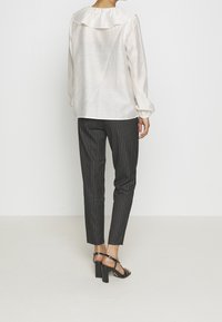 Blouse blanche texturée avec un large col volé ; associée à un pantalon noir à rayures verticales et des sandales à talons noires.