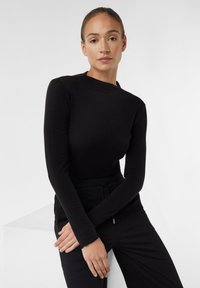 Maglietta nera a maniche lunghe realizzata in un tessuto leggero, caratterizzata da un collo alto e da una vestibilità aderente, indossata con pantaloni neri. Aspetto semplice ed elegante.
