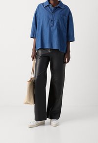 Königsblaues Denim-Übergrößenhemd mit Knopfleiste und Brusttasche, kombiniert mit schwarzen, weiten Lederhosen und weißen Sneakers. Beiger Tragetasche.