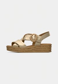 Sandale compensée beige avec brides croisées, boucle ronde sur le côté et semelle texturée, vue de profil extérieur sur fond uni.