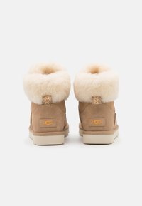 Hellbraune Wildleder-Ankle Boots mit flauschigen, beigen Schaffell-Bündchen. Ausgestattet mit einer kleinen Schlaufe hinten und einem orangefarbenen UGG-Logo an der Seite. Flache Gummisohlen.