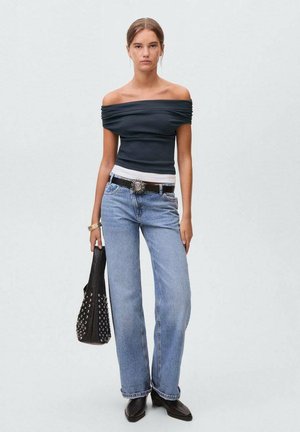 Off-the-shoulder dark top with gathered fabric, paired with light blue wide-leg jeans. Accessories include a studded black bag and silver belt.