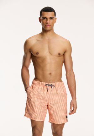 Shorts de bain pour hommes en orange avec un motif ondulé blanc, taille élastique, cordon de serrage et poches latérales. Le matériau semble léger et respirant.