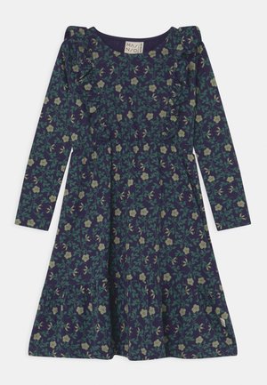 Mørkeblå langærmet kjole med grønt blomsterprint, flæser på bryst og skuldre samt en samlet, lagdelt nederdel.