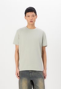 Ανοιχτό γκρι κοντομάνικο μπλουζάκι με υφασμάτινο σχέδιο, στρογγυλή λαιμόκοψη και χαλαρή γραμμή, σε συνδυασμό με ξεθωριασμένα τζιν παντελόνια.