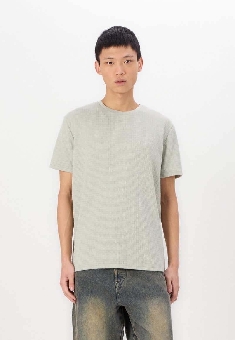 Ανοιχτό γκρι κοντομάνικο μπλουζάκι με υφασμάτινο σχέδιο, στρογγυλή λαιμόκοψη και χαλαρή γραμμή, σε συνδυασμό με ξεθωριασμένα τζιν παντελόνια.