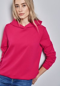 Sweatshirt fuchsia avec capuche, fabriqué en tissu lisse, avec une coupe décontractée et des manches longues. Design simple sans motifs visibles.