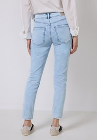 Jasnoniebieskie dżinsowe spodnie skinny z wysokim stanem, pięcioma kieszeniami i tonowanym przeszyciem. Noszone z casualowymi sneakersami, o gładkiej teksturze.