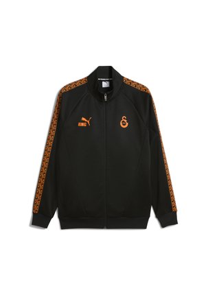 Veste zippée noire avec logo Puma orange, texte "KING", emblème du club sur la poitrine et rayures géométriques orange le long des manches.