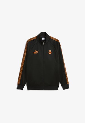 Schwarze Zip-Jacke mit orangefarbigem Puma-Logo, "KING"-Text, Vereinswappen auf der Brust und orangefarbigen geometrischen Mustern an den Ärmeln.