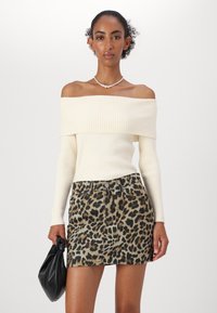 Slonový off-shoulder rebrovaný pletený top v kombinácii s krátkou džínsovou sukňou s leopardím vzorom, ktorá má päť vreciek a predné zapínanie na gombík.