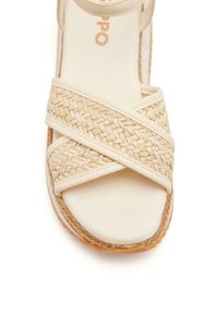 Sandale espadrille tissée en crème. Elle présente des sangles entrecroisées, une semelle lisse et une base texturée inspirée du jute. Design léger et décontracté.