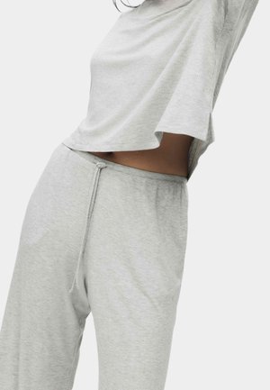 Mujer con top corto de punto acanalado gris claro y pantalones a juego con cordón, frente a un fondo claro y sencillo.